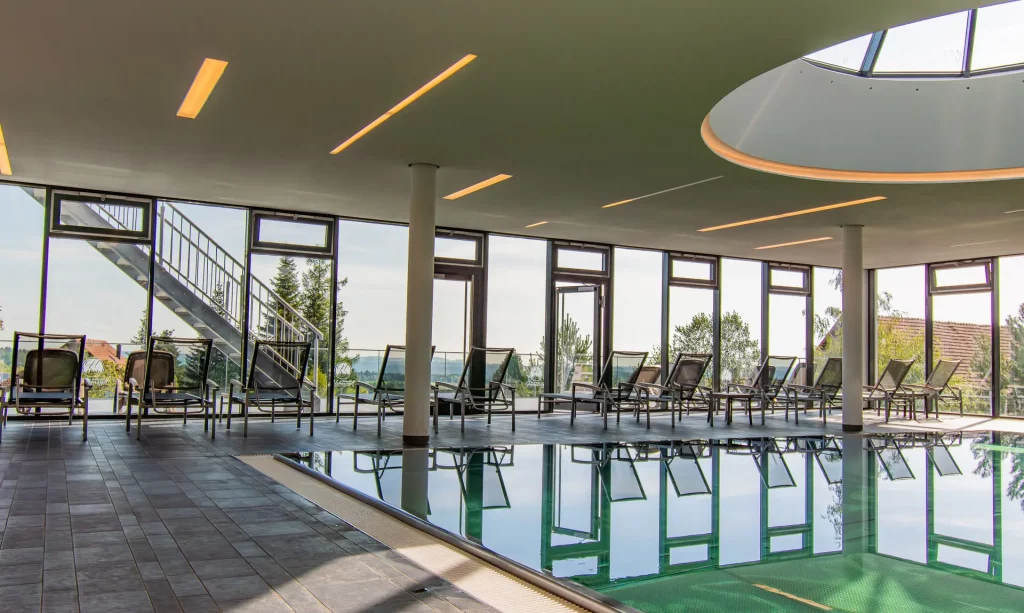 Entspannte Atmosphäre im Poolbereich mit bequemen Relaxliegen vor großzügiger Fensterfront und natürlichem Lichteinfall