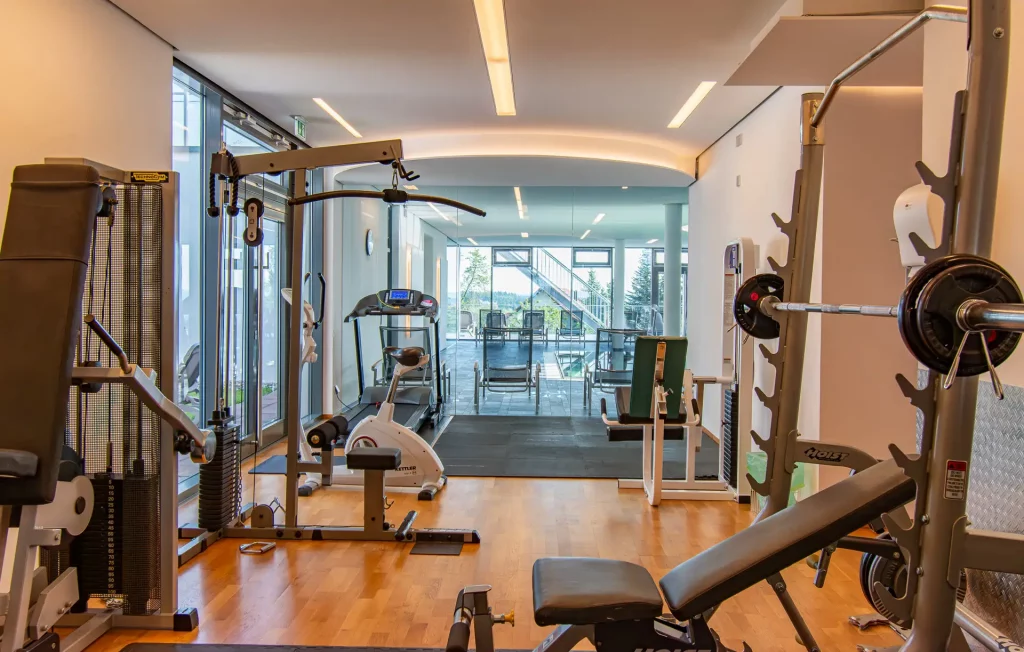 Wellness-Fitnessraum im Wellnesshotel Hohenrodt mit modernen Trainingsgeräten und Blick auf Poolbereich